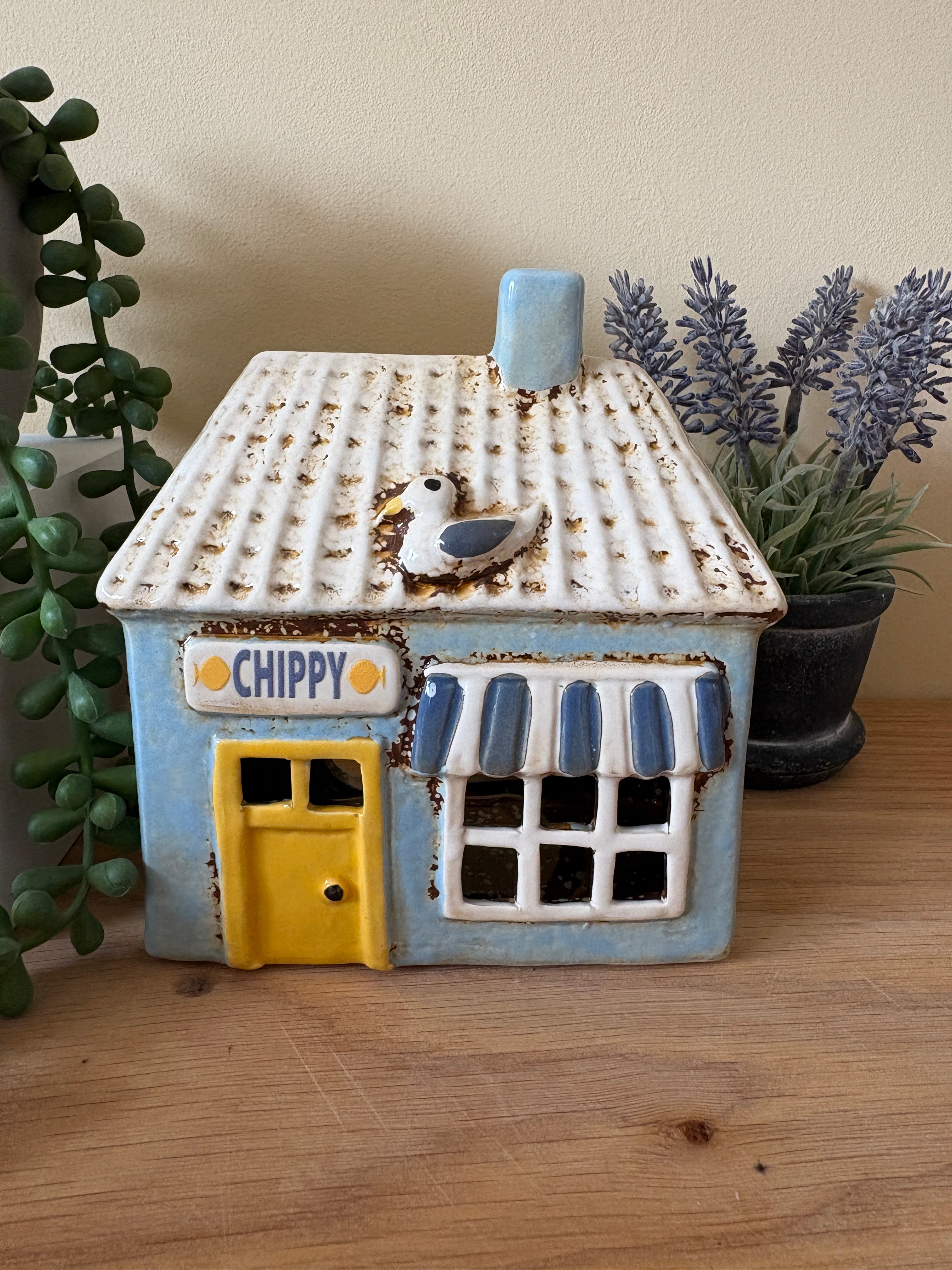 Decorative house-shaped tea light with a yellow door and blue accents on a wooden surface.