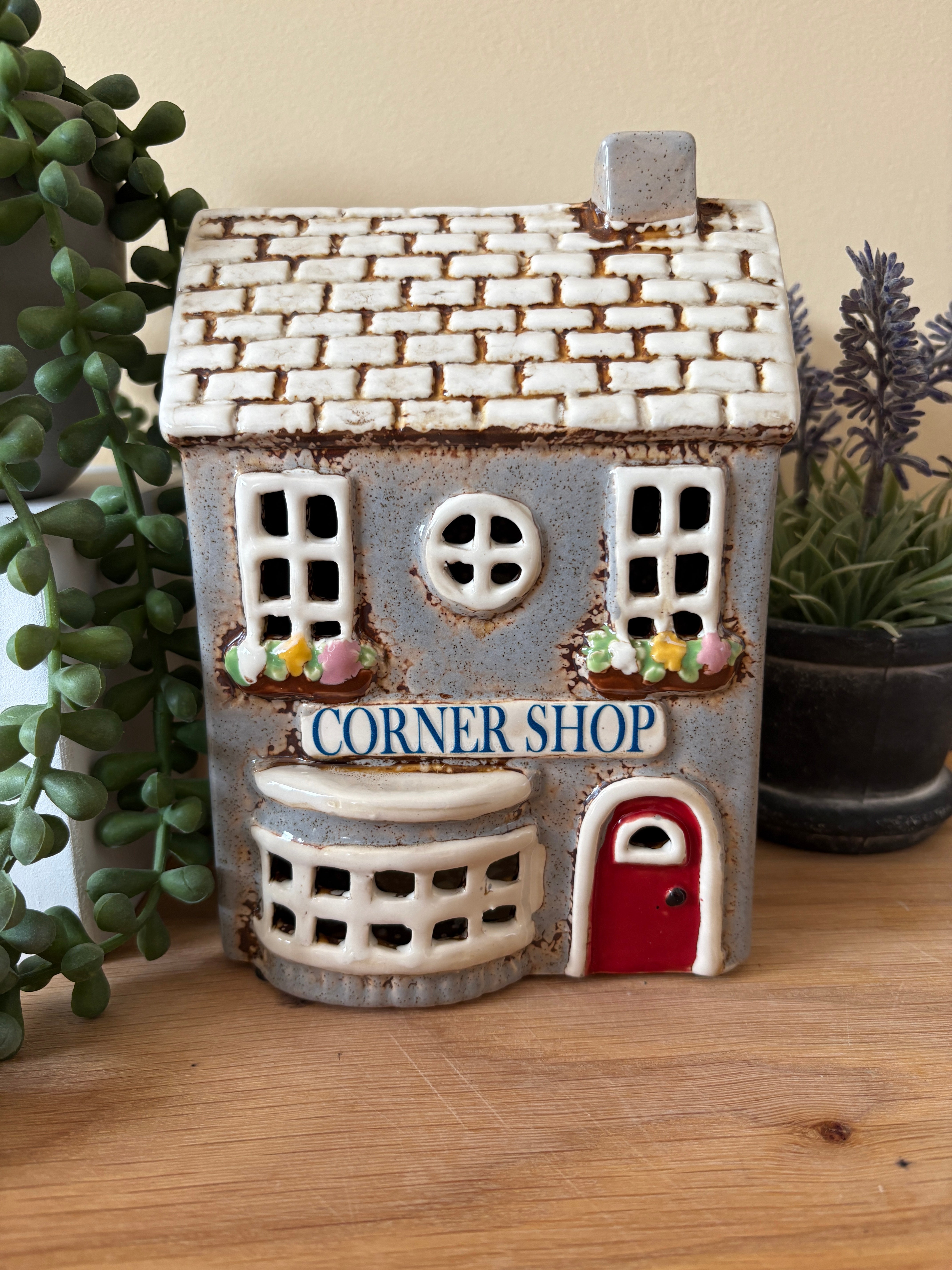 Ceramic house-shaped sign with 'Corner Shop' on a wooden surface