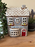 Ceramic house-shaped sign with 'Corner Shop' on a wooden surface